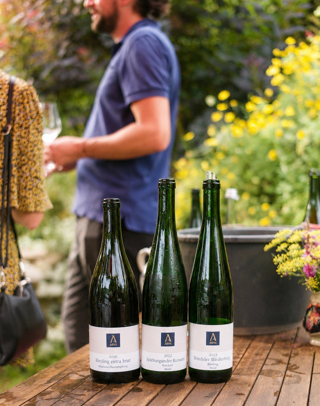 Drei ARNS Weinflaschen (Riesling extra brut, Spätburgunder Rotwein trocken, Briedeler Weißerberg Riesling) bei einer Weinprobe im Freien am Weingut Arns in Reil an der Mosel